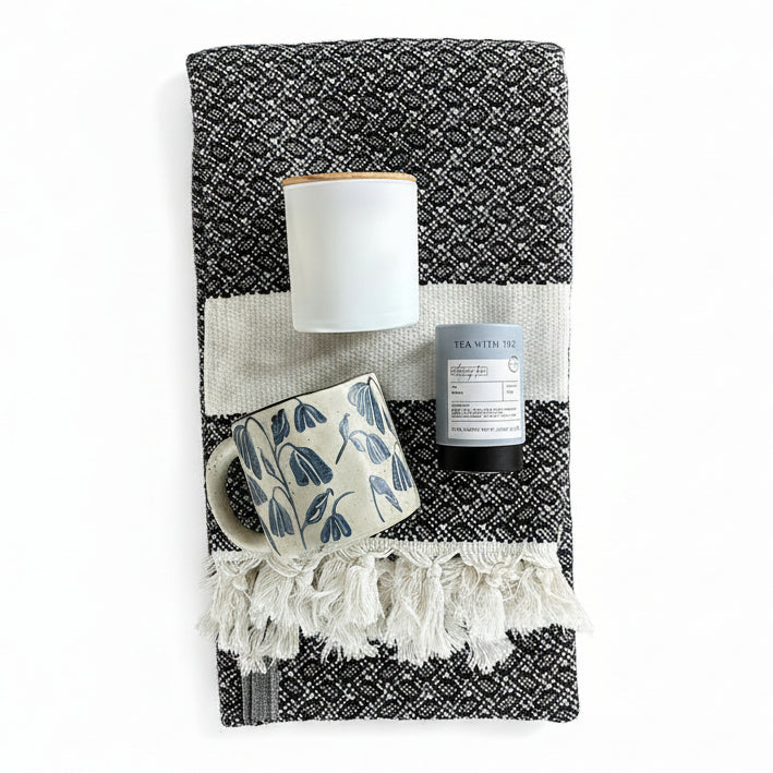 Black and White patterned cotton turkish throw blanket with tea, a floral blue and white mug, and a matte white and wood soy candle.
