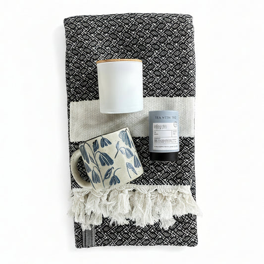 Black and White patterned cotton turkish throw blanket with tea, a floral blue and white mug, and a matte white and wood soy candle.